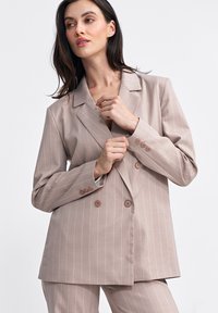 Dwurzędowa marynarka w jasnym beżu z białymi pionowymi paskami, z klapami w stylu wyściełanym i pięcioma guzikami na rękawach.
