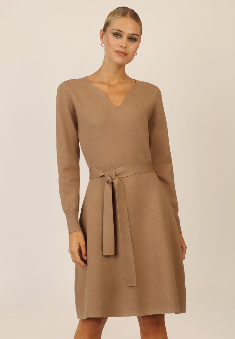 Braunes Strickkleid mit langen Ärmeln, V-Ausschnitt und einem Taillenband. Glatte Textur und A-Linie, die bis über die Knie reicht.
