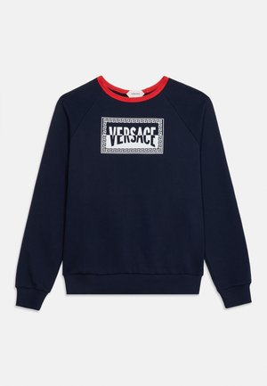 Sweat-shirt bleu marine manches longues avec col rouge et logo blanc Versace encadré par un motif géométrique sur la poitrine.