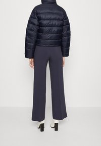 Tmavě modrá péřová bunda s krátkým střihem a prošívanou texturou, doplněná tmavými širokými kalhotami a bílými kotníkovými botami na podpatku.