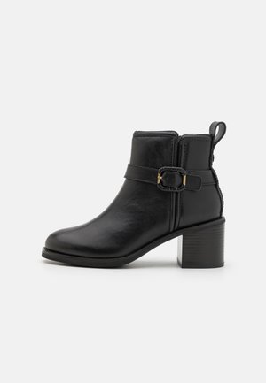 Bottines noires en cuir lisse, avec un talon carré et une sangle décorative dotée d'une boucle dorée. Fermeture à glissière sur le côté.