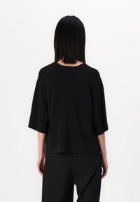 Top de malha preto com mangas curtas e um corte relaxado, apresentando um brilho subtil e um tecido texturizado, combinado com calças pretas a condizer.