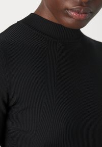 Top negro de manga larga con cuello alto, que presenta un tejido texturizado y costuras verticales para una silueta ajustada.