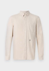 Camicia beige a maniche lunghe con colletto bottonato, taschino sul petto e piccole lettere nere ricamate vicino alla parte inferiore anteriore.