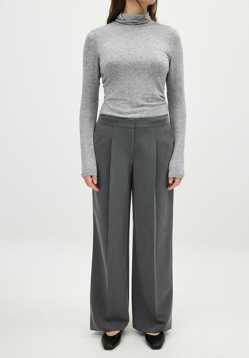 Pelēks gariem piedurknēm turtlenecks tops apvienots ar augsto jostasvietu pelēkiem plašiem biksēm, kas rotātas ar smalkiem svītriņām un elegantiem melniem apaviem.