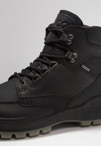 Bota de senderismo de cuero negro con superficie texturizada, ojales de metal y etiqueta impermeable. Suela de goma gruesa con un dibujo pronunciado.