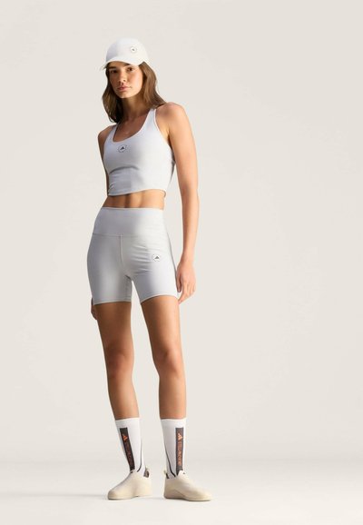 Vaaleanharmaa urheiluasu, joka sisältää lyhyen toppimaisen t-paidan ja korkeavyötäröiset shortsit, täydentäen asua yhteensopivalla lippiksellä ja valkoisilla sukilla, joissa on kontrastivärit.