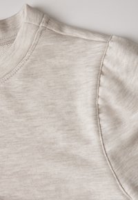Felpa corta a maniche corte color beige chiaro con scollo rotondo. Il tessuto presenta una sottile trama con dettagli di cucitura lungo i bordi.