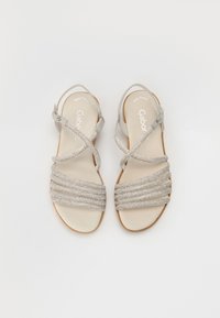 Silver strappy sandals with a flat sole, featuring multiple braided bands and a suede ankle strap with a buckle. Smooth leather footbed.