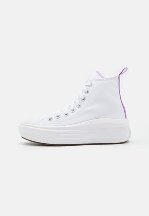 Białe wysokie sneakersy z grubą podeszwą, białymi sznurowadłami i fioletową pętelką na pięcie na jednolitym białym tle.