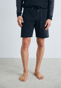 Black cotton shorts with an elastic waistband and drawstring, featuring textured patterned accents along the sides.