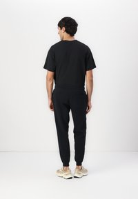 T-shirt negru din bumbac și pantaloni de trening bleumarin, cu mansete elastice și detaliu cu buzunar pe spate. Adidași bej completează ținuta.