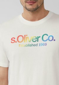 Witte katoenen t-shirt met een gegroepeerd multicolor logo "s.Oliver Co." en de tekst "Opgericht in 1969" over de borst.