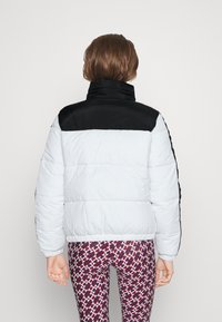 Kurtka puchowa z białym korpusem i czarnymi ramionami. Posiada wysoki kołnierz, pikowaną teksturę i ściągacze przy mankietach. W komplecie z legginsami w wzory.