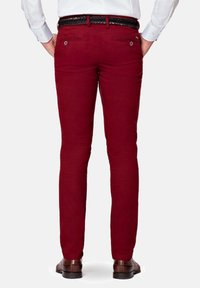 Červené bavlněné chinos kalhoty se slim fit, dvěma zadními kapsami a texturovaným pleteným pásem. Na sobě má hnědé boty na světlém pozadí.