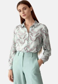 Light blue patterned blouse with gray and white wavy designs, button-down front, long sleeves, paired with light blue high-waisted pants.