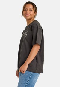 Camiseta oversized gris oscuro de algodón, con mangas cortas, escote redondo y un estampado gráfico en el frente. Ajuste casual.