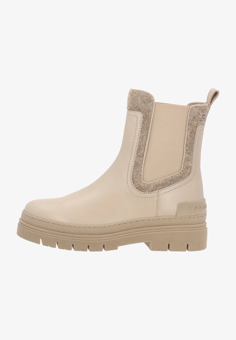 Botte Chelsea beige avec semelle épaisse à rainures, panneau latéral élastique, bordure en laine, languette de traction, et logo embossé sur le talon.