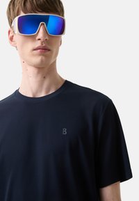 Mørkeblå t-shirt med kort ærme og et diskret præget "B" logo, parret med hvide solbriller med blå spejlglas.