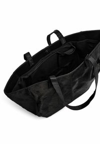 Fekete tote táska szőrméből, bőr kiegészítőkkel. Tágas belső térrel és két erős füllel rendelkezik a hordozáshoz. Záródás nem látható.