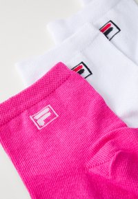 Drei Paar Socken: ein pinkes mit einem Logo-Patch und zwei weiße. Die Socken haben ein strukturiertes Strickdesign und bunte Logoakzente.