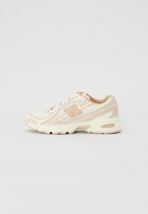 Beige og hvid mesh-sneaker med tyk sål, snørebånd og logo på siden, vist i profil på en ensartet lys baggrund.