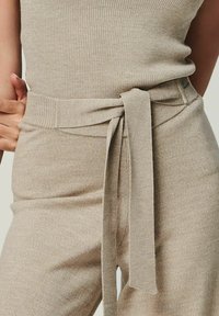 Beige ribbed knit outfit featuring a fitted top and high-waisted pants with a matching tie belt. Smooth texture and minimal design details.