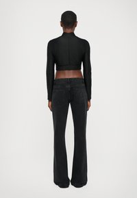 Black cropped long-sleeve top with a high neck and elastic waistband paired with black flared jeans featuring back pockets and logo detail.