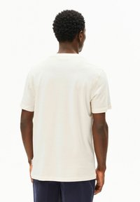 Roomkleurig katoenen T-shirt met korte mouwen en een ronde halslijn, voorzien van een label aan de linkerkant nabij de zoom. Soepele textuur.