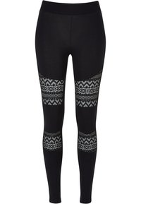Leggings noirs avec une taille haute, présentant des découpes décoratives à motifs sur les côtés. Le matériau a une texture lisse.