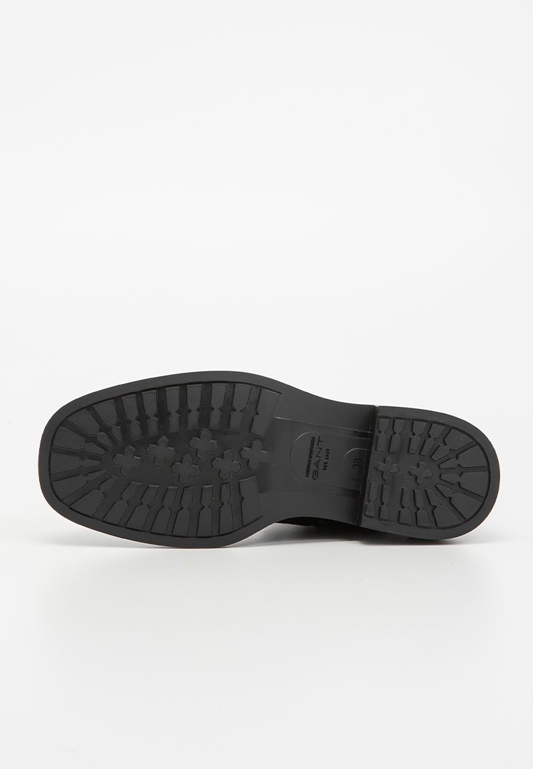 Suela de bota de goma negra con un patrón de relieve texturizado que presenta ranuras y elementos elevados para un mejor agarre, etiquetada con detalles del fabricante.