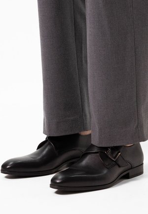 Zwarte leren schoenen met een spitse neus en een zijgespannetje. Draag ze met grijs taps toelopende broeken, die een gladde textuur en een minimaal ontwerp laten zien.