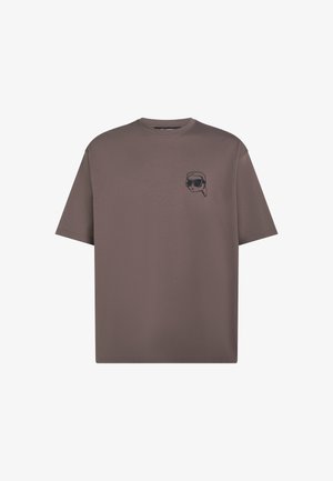 T-shirt marron à manches courtes avec un petit cartoon noir brodé portant des lunettes de soleil et une écharpe sur le côté gauche de la poitrine.