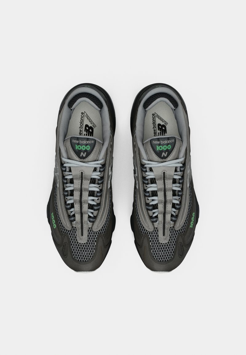 Baskets de sport grises avec des panneaux en mesh, des accents texturés et des semelles en caoutchouc noir. Présente des éléments réfléchissants et un système de laçage distinct.