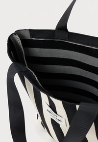 Torebka typu tote w czarno-białe paski z zewnętrzną częścią wykonaną z płótna, zamknięciem na zamek oraz podszewką z tkaniny w poziome paski. Widoczna metka z logo.