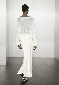 Maglione bianco lavorato a maglia con una vestibilità ampia e maniche lunghe, abbinato a una lunga gonna coordinata. Entrambi presentano dettagli con lacci.