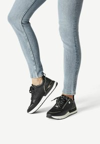 Chaussures de sport noires avec une tige texturée ornée d'accents scintillants et une semelle blanche. Le design comprend des lacets noirs et des fermetures éclair latérales.