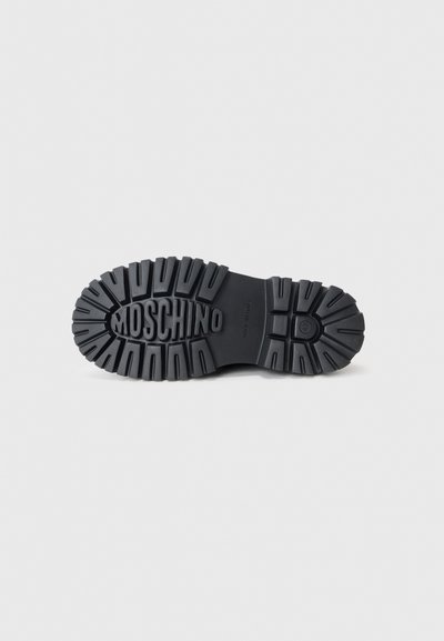 Svart gummistövle sula med djup mönstring, med "Moschino" präntat på mellandelen och olika mönster för grepp.