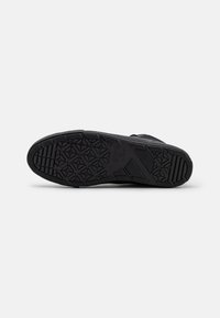 Zwarte sneakersole met geometrisch loopvlakpatroon en textuur voor grip, gefotografeerd tegen een effen witte achtergrond.