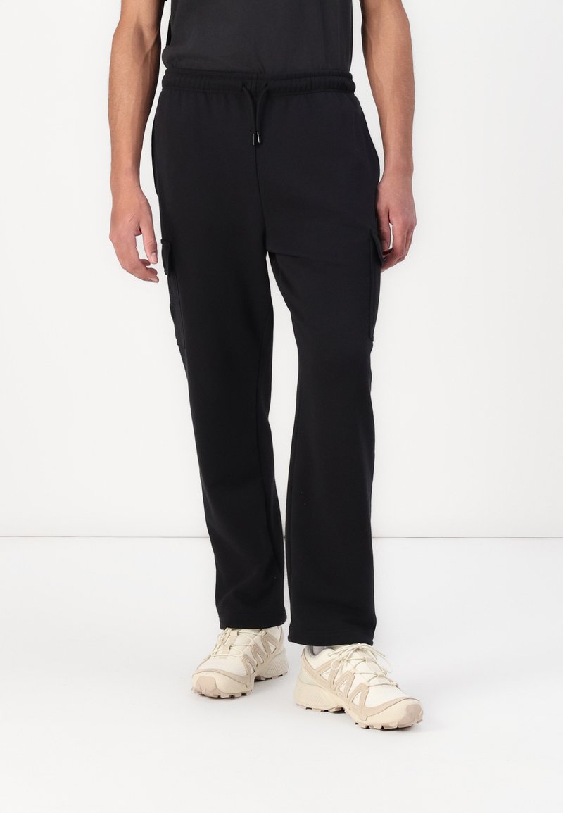 Black cargo pants made of soft fabric, featuring an elastic waistband, side pockets, and a relaxed fit. Paired with light-colored athletic shoes.