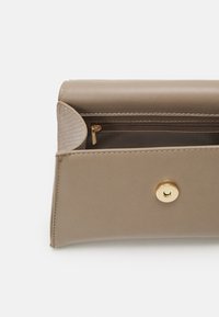 Piccola pochette taupe aperta, che mostra la chiusura a scatto dorata e una tasca interna con zip, dotata di un pannello laterale testurizzato.