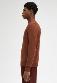 Maglione marrone a maniche lunghe in un punto di maglia testurizzato, con collo rotondo e polsini e orlo a coste, indossato con pantaloni scuri coordinati.