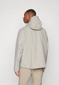 Lichtgrijze hoodie-jack met een gladde textuur en elastische manchetten, met een ontspannen pasvorm en gedetailleerde stiksels. Achteraanzicht weergegeven.