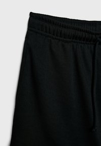 Pantalons de survêtement noirs avec une taille élastique, des détails de cordon de serrage et une texture de tissu douce. Design simple sans motifs visibles.