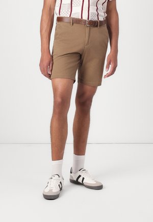 Shorts en coton marron à coupe droite, accompagnés d'une ceinture marron. Le modèle porte des chaussettes blanches et des baskets à rayures grises.