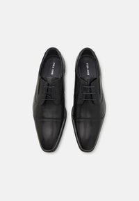 Pantofi de piele negri cu un finisaj lustruit, vârf ascuțit și șireturi cu patru orificii. Prezintă cusături subtile și o textură netedă.