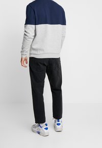 Sudadera gris y azul marino con un diseño a bloques de color, combinada con pantalones negros y zapatillas grises con detalles azules.