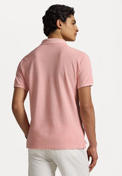 Tricou polo dintr-un material moale, texturat, de culoare roz deschis; are un guler la gât și mâneci scurte, cu slituri laterale la tiv.