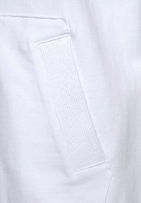 Weißes Sweatshirtmaterial mit einer strukturierten aufgesetzten Tasche, die gerippte Details aufweist. Die Oberfläche ist glatt mit einem leichten Glanz.