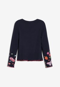 Marineblauses mit langen Ärmeln, verziert mit bunten Blumen- und Schmetterlingsmustern auf den Ärmeln, abgerundet mit einem gewellten rosa Saumdetail. Aus weichem Baumwollmaterial.